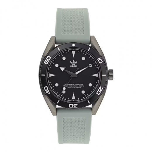 Reloj analógico deportivo Adidas Edition Two con correa de silicona gris claro y caja gris oscuro mate. El dial negro destaca con el logotipo del trébol y un bisel de buceo con números blancos. Se muestra sobre un fondo sofisticado junto a su estuche oficial de cuero.