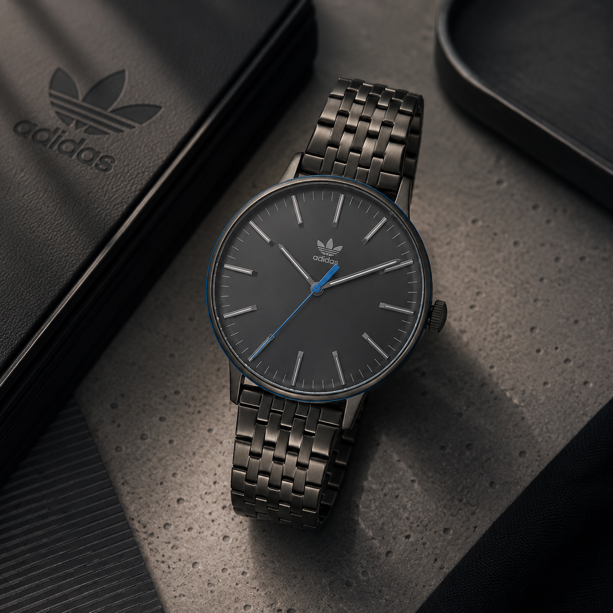 Reloj de mujer Adidas Code One AOSY22023 con caja ultraplana de acero gris antracita, dial negro minimalista con segundero azul y brazalete de eslabones articulados.